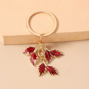 Exquisite gold keychain with red enamel maple leaves on a warm aesthetic background