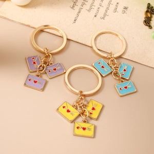 Three colorful enamel envelope keychains with heart patterns on a warm beige background