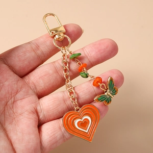 Detailed view of handmade butterfly and heart enamel keychain held in a model's hand