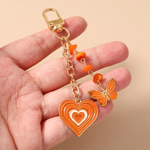 Detail of golden heart and butterfly keychain with orange stones held in hand