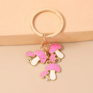 Dettaglio portachiavi dorato con pendenti a fungo in smalto rosa e bianco su sfondo beige