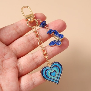 Close-up of blue enamel butterfly and heart keychain held in hand with gold hardware