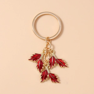 Detail of golden keychain with six vibrant red enamel leaf pendants on a smooth surface