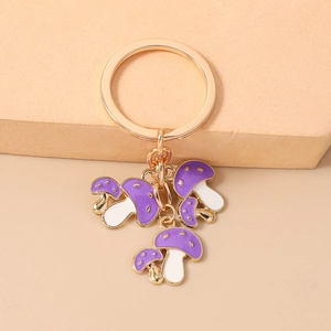 Dettaglio di un portachiavi dorato con funghi viola in smalto e gambi bianchi decorati