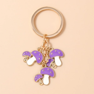 Dettaglio di portachiavi a fungo viola con anelli dorati e pois bianchi su sfondo rosa