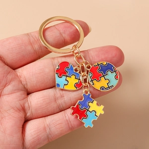 Dettaglio del portachiavi dorato con ciondoli a forma di cuore a puzzle colorato in mano