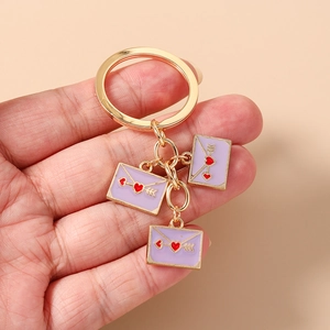 Detailed view of hand-held golden keychain with purple enamel heart envelopes