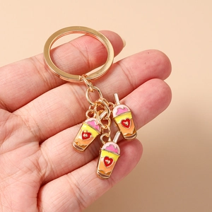 Detail of three colorful heart milk tea charms on a gold keychain being held