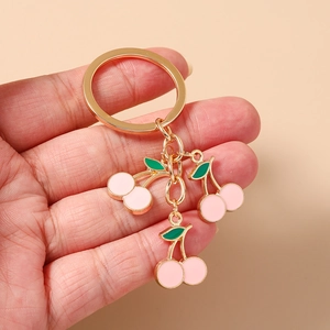 Dettaglio dei ciondoli a ciliegia rosa su un portachiavi dorato tenuto su sfondo beige