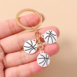 Détail d'un porte-clés doré avec trois breloques de basket blanches tenu dans une main