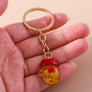 Detail of a red glove-shaped keychain with gold glitter and heart charm held by hand