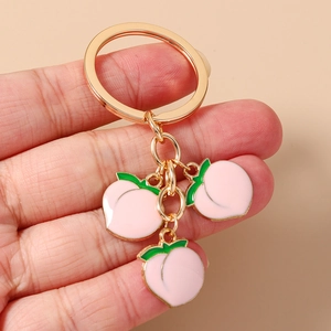 Detailed macro shot of a golden peach keychain featuring three pink enamel fruit pendants