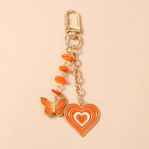Detail of orange butterfly charm keychain with gold chains and layered resin heart pendant