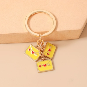 Close-up of golden heart envelope charms on a key ring against an beige background