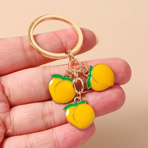 Detail of golden keychain with three yellow enamel peach charms held in hand