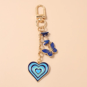 Detail of golden keychain featuring blue butterfly and layered enamel heart pendant charm