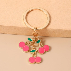 Dettaglio portachiavi a ciliegia rosa con finiture dorate su espositore beige elegante
