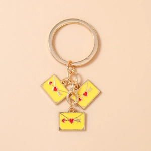 Close-up of golden alloy keychain with yellow enamel envelope charms and red heart arrow detail