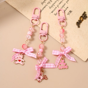 Pink beaded bear and heart bag charms with fabric bow on beige vintage desktop background