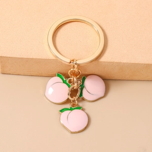 Detailed view of three peach charms with pink enamel and gold-tone metal keyring