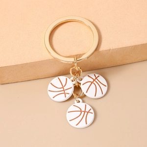 Détail du porte-clés doré avec trois breloques de basket blanches sur un support beige