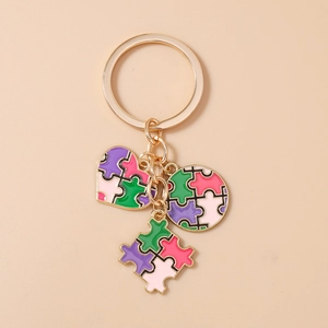 Dettaglio portachiavi dorato a cuore e pezzo di puzzle con smalto colorato vivace
