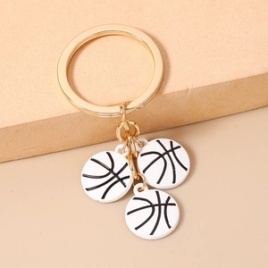 Détail d'un porte-clés doré avec trois breloques de basket-ball blanches sur socle beige