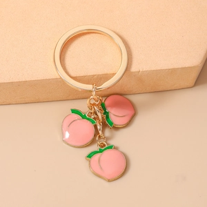 Close-up of golden keychain featuring three realistic pink peach pendants and green leaves