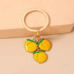 Detailed view of golden metal keychain with three yellow enamel peach charms and leaves