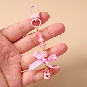 Detailed shot of pink beaded keychain with fabric bow and heart charm held in hand