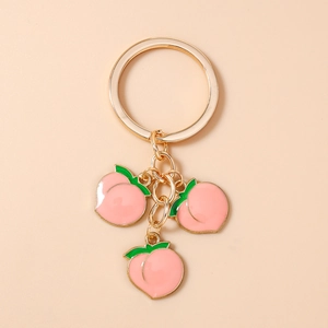 Detail of peach pendants on a gold keychain with pink enamel finish and green leaf accents