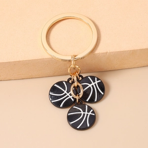Détail d'un porte-clés basketball doré avec trois pendentifs en émail noir sur socle beige