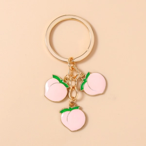 Detail of golden keychain featuring three pink peach enamel charms with green leaves