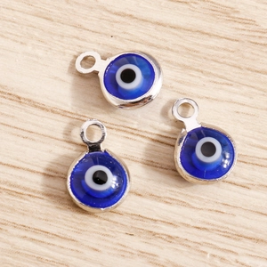 DIY blue glass evil eye charms with silver metal edges for jewelry making on wood surface