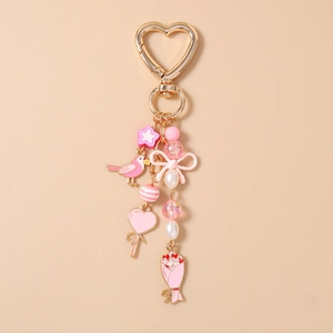 Detailed close-up of pink bird, heart lollipop, and flower enamel charms on a gold keychain