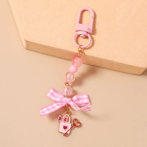 Detailed close-up of pink beaded keychain with fabric bow and enamel charms on a stone