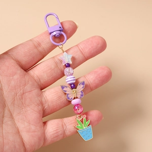 Détail du porte-clés perlé avec papillon violet et pendentif cactus bleu en main