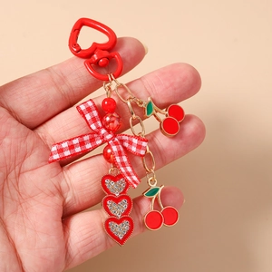 Macro shot of red heart clasp and cherry bow keychain with rhinestones in hand