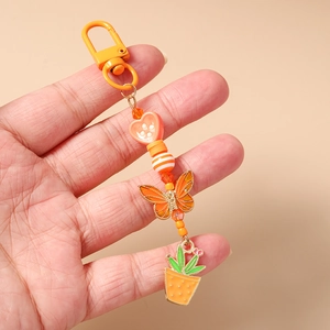 Détail d'un porte-clés à perles orange avec charms cœur, papillon et cactus en main