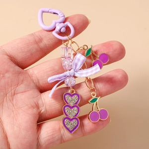 Close-up of purple cherry keychain with heart rhinestones and a bow on pink background