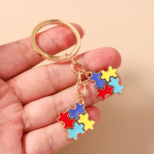 Gros plan de porte-clés en pièces de puzzle dorées avec émail coloré tenus à la main