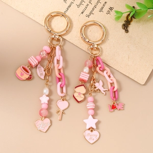 Pink beaded star keychain with heart pendants and gold spring clasp on a warm background