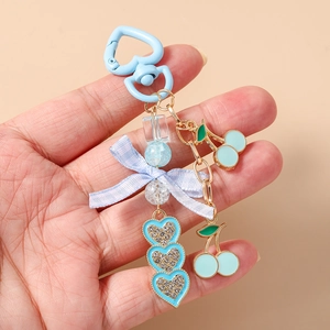 Detail view of sky blue heart keychain with ribbon bow and cherry pendants in hand