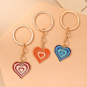 Trois porte-clés en forme de cœur colorés avec anneaux dorés sur fond beige neutre