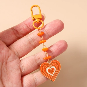 Vue détaillée d'un porte-clés cœur en émail orange avec chaîne perlée tenu à la main