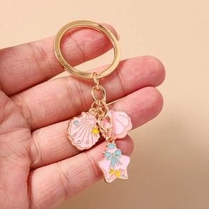 Detail of pink enamel starfish and seashell keychain held by hand for scale reference