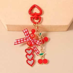 Detail of red cherry keychain with heart charms, plaid bow, and polished enamel finish