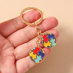 Détail d'un porte-clés doré avec pendentifs de cœur en puzzle colorés tenu en main