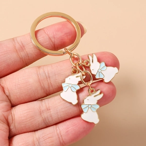 Détail rapproché du porte-clés doré avec lapins en émail blanc et nœuds bleus élégants