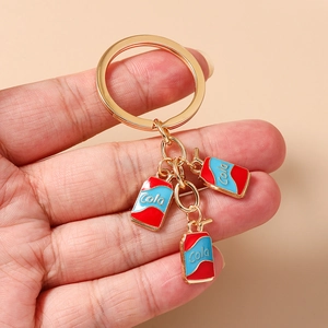 Detail of mini Cola can charms on a golden keychain held to show scale and texture